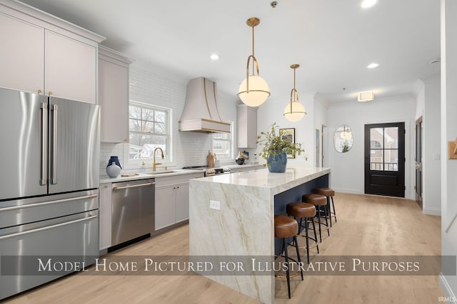 kitchen with pendant lighting, stainless steel appliances, custom range hood, white cabinetry, and a kitchen island