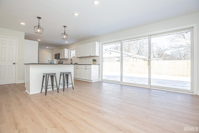 6400 Jefferson Ave, Evansville, IN 47715 - kitchen with pendant lighting, dark countertops, stainless steel microwave, light wood-style floors, and white cabinetry