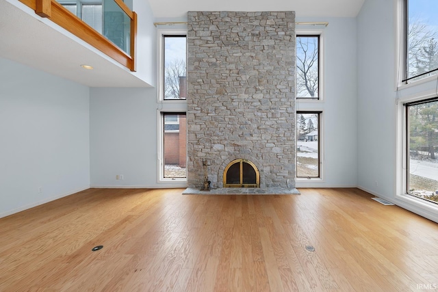 unfurnished living room featuring light wood-type flooring, a high ceiling, baseboards, and a stone fireplace