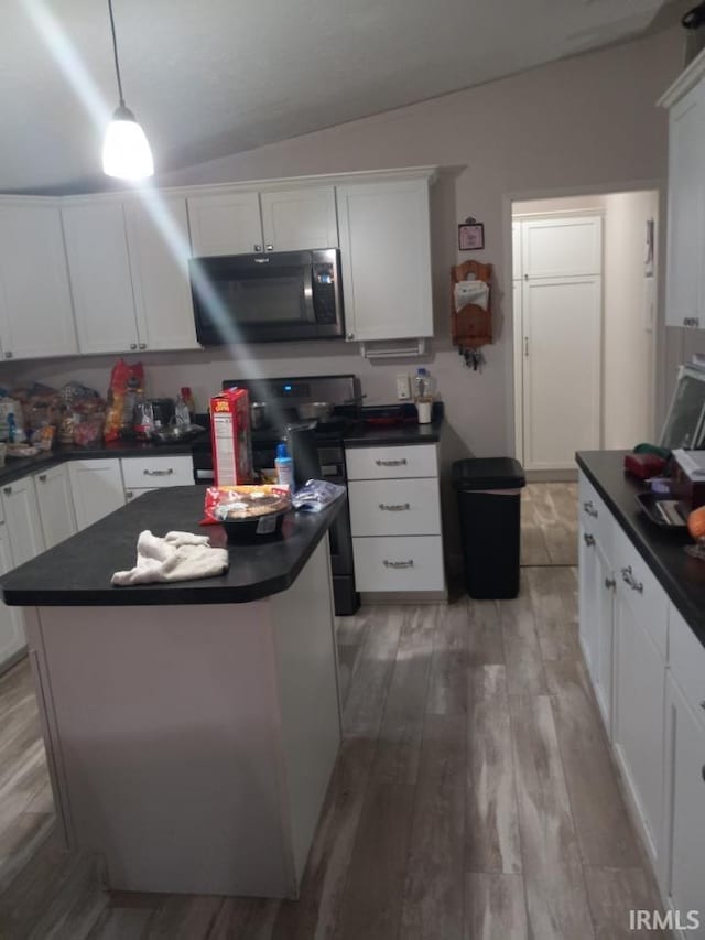 kitchen featuring hanging light fixtures, stainless steel microwave, dark countertops, and white cabinetry