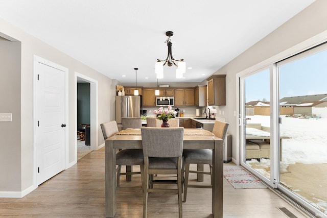 dining room with light wood-type flooring, baseboards, and an inviting chandelier