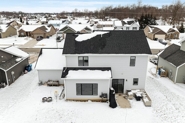 snow covered house featuring a residential view, central AC, and roof with shingles