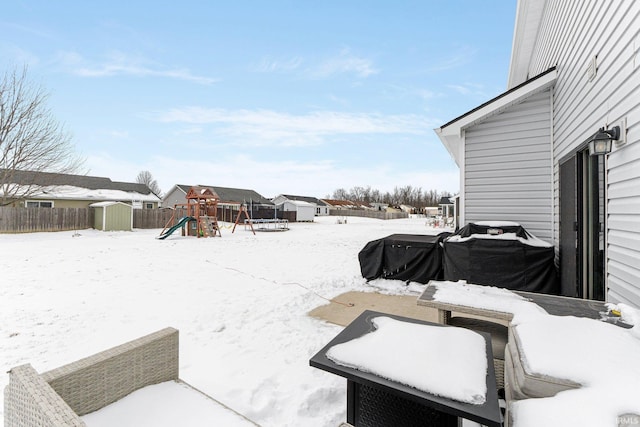 yard covered in snow with an outbuilding, a playground, fence, and a storage shed