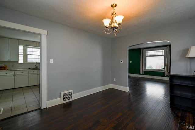 unfurnished dining area featuring baseboards, visible vents, arched walkways, dark wood-type flooring, and a notable chandelier