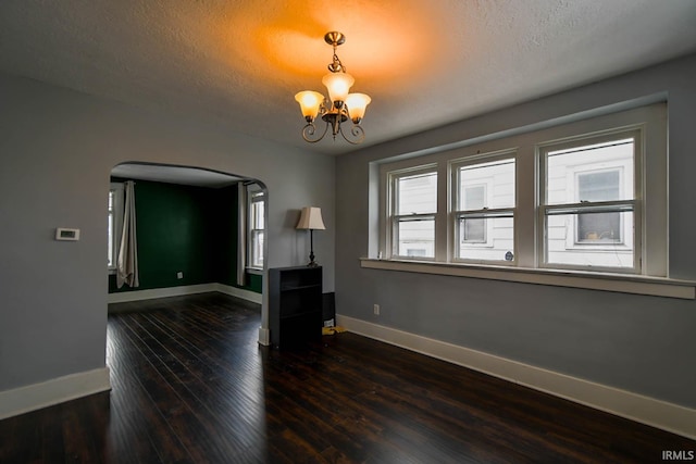 empty room featuring baseboards, arched walkways, dark wood-style floors, a textured ceiling, and a notable chandelier