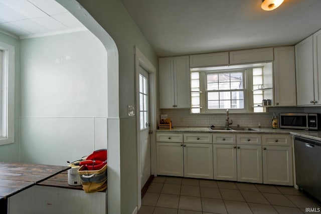 kitchen with white cabinets, decorative backsplash, light stone countertops, stainless steel appliances, and a sink