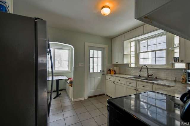 kitchen with light tile patterned floors, a sink, white cabinets, black appliances, and tasteful backsplash