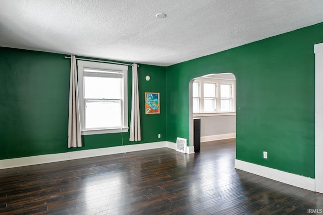 unfurnished room with a textured ceiling, baseboards, arched walkways, and dark wood-style flooring