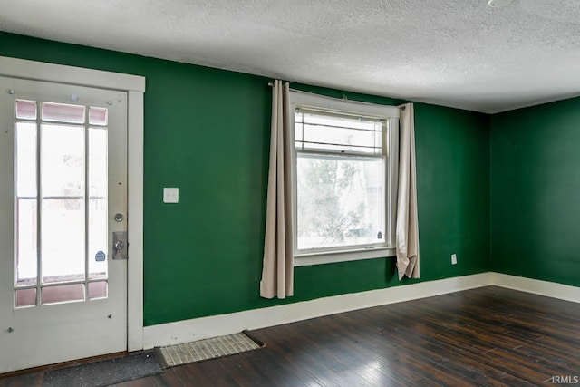 empty room with dark wood-style flooring, a textured ceiling, and baseboards