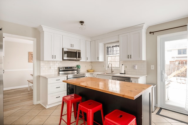 kitchen featuring appliances with stainless steel finishes, white cabinetry, butcher block countertops, and a kitchen breakfast bar