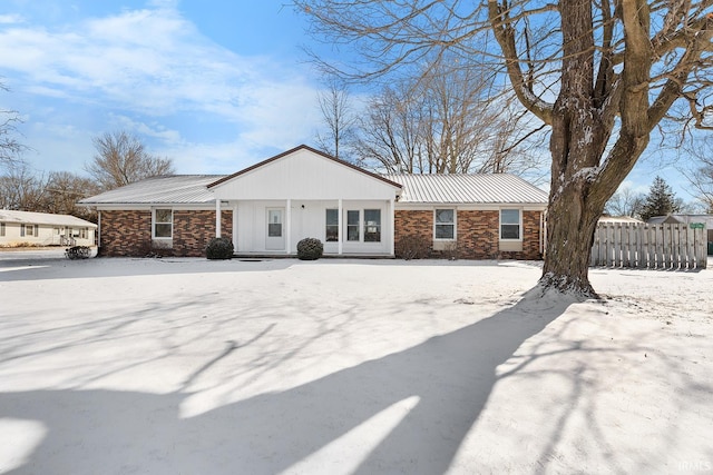 ranch-style home featuring metal roof, brick siding, and fence