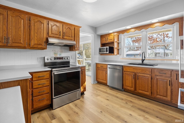 kitchen featuring brown cabinets, stainless steel appliances, light countertops, a sink, and under cabinet range hood