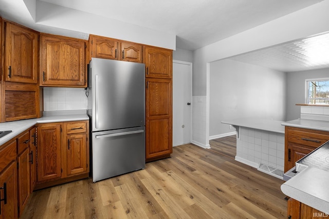 kitchen with visible vents, light countertops, freestanding refrigerator, brown cabinets, and light wood finished floors