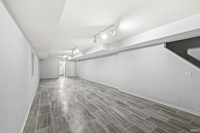 finished below grade area with wood finish floors, rail lighting, a textured ceiling, and baseboards