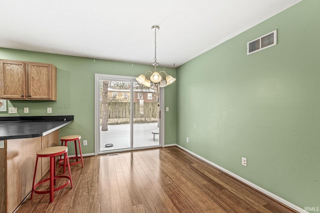 unfurnished dining area featuring dark wood-style floors, baseboards, visible vents, and a notable chandelier