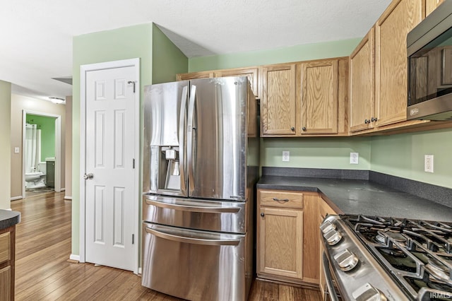 kitchen with light wood finished floors, dark countertops, appliances with stainless steel finishes, a textured ceiling, and baseboards