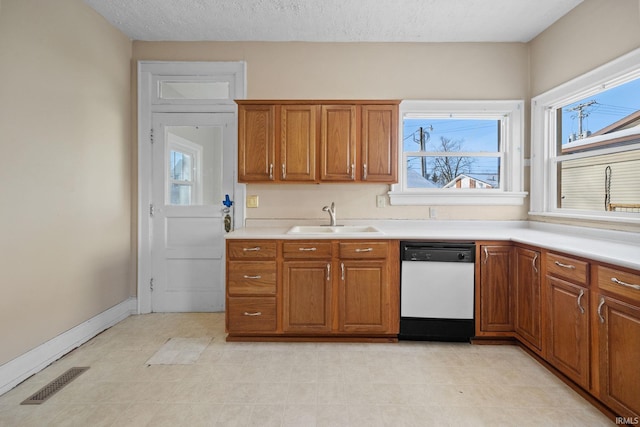 kitchen with brown cabinets, light countertops, visible vents, white dishwasher, and a sink