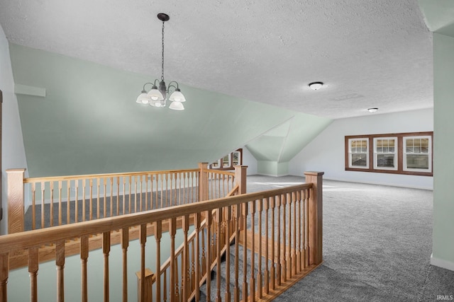 corridor featuring a textured ceiling, a chandelier, carpet flooring, an upstairs landing, and vaulted ceiling