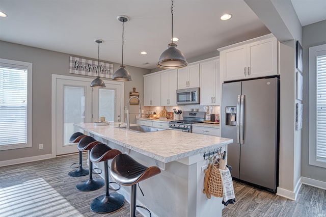 kitchen with appliances with stainless steel finishes, white cabinets, light countertops, and an island with sink