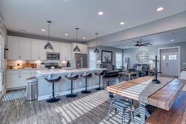 kitchen featuring white cabinets, appliances with stainless steel finishes, a breakfast bar, hanging light fixtures, and a kitchen island with sink