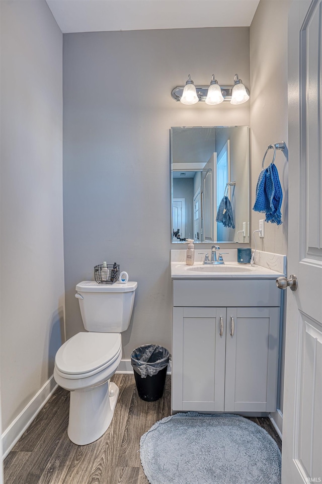 half bath with baseboards, vanity, toilet, and wood finished floors