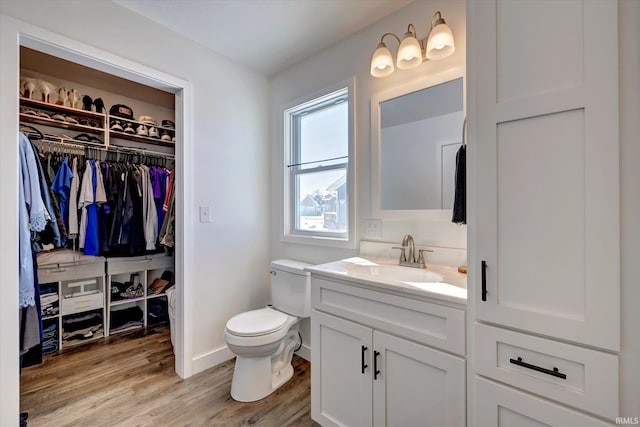 bathroom featuring toilet, wood finished floors, vanity, baseboards, and a spacious closet