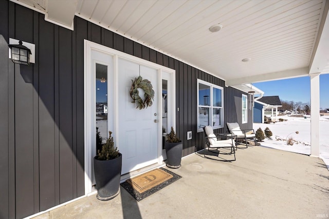 snow covered property entrance featuring board and batten siding and a porch