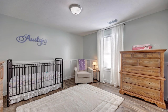 bedroom with a nursery area, visible vents, and wood finished floors