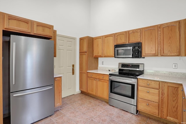 kitchen with light tile patterned floors, a high ceiling, appliances with stainless steel finishes, and light countertops