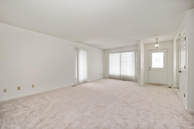 unfurnished living room with a chandelier, light carpet, and baseboards