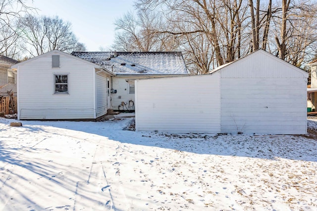 snow covered back of property with a shingled roof and a detached garage