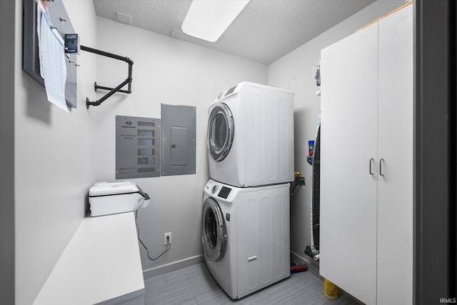 laundry room featuring a textured ceiling, laundry area, stacked washer and dryer, baseboards, and electric panel