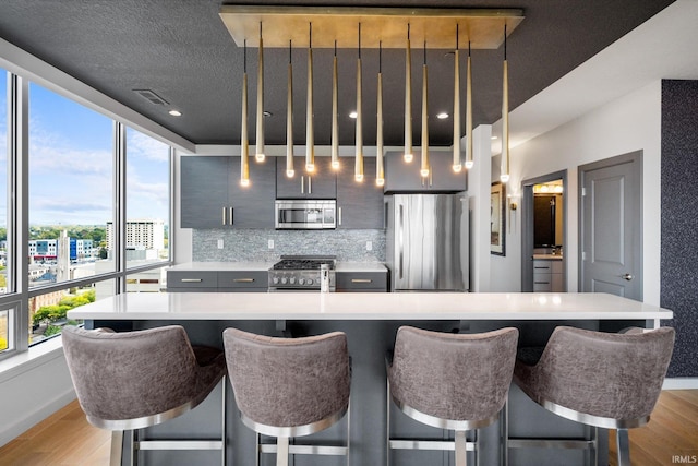 kitchen featuring stainless steel appliances, light countertops, decorative light fixtures, and a kitchen breakfast bar