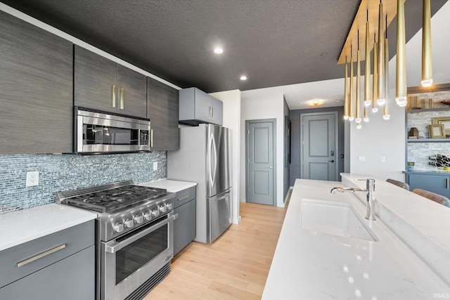 kitchen with light wood-style flooring, a sink, appliances with stainless steel finishes, light stone countertops, and decorative light fixtures