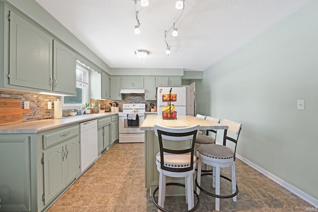 kitchen featuring tasteful backsplash, light countertops, a sink, white appliances, and under cabinet range hood