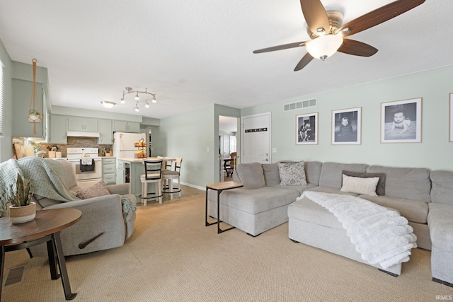 living area with baseboards, a ceiling fan, visible vents, and light colored carpet