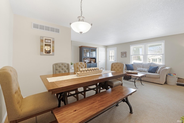 carpeted dining room featuring visible vents and a textured ceiling