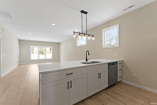 kitchen featuring a peninsula, a sink, open floor plan, light countertops, and dishwasher