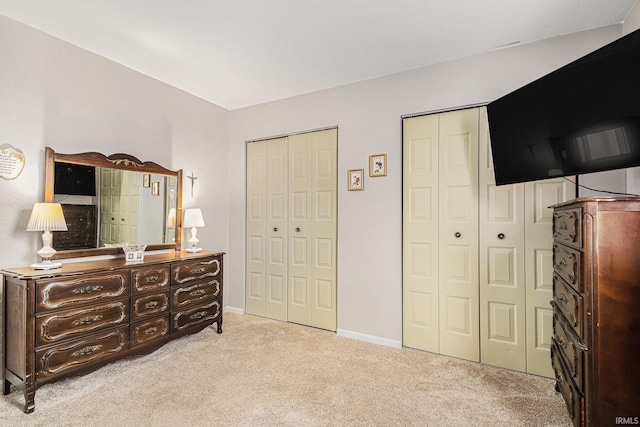 bedroom featuring baseboards, light colored carpet, and multiple closets