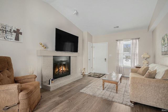 living room featuring vaulted ceiling, visible vents, a fireplace, and wood finished floors