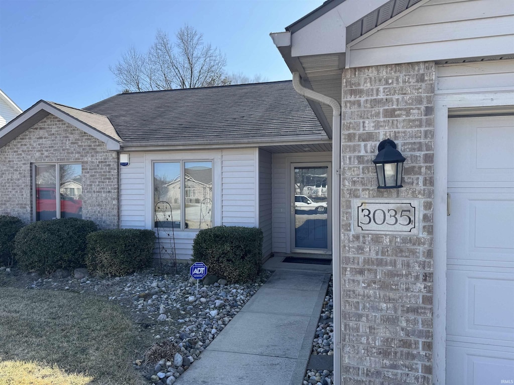 property entrance with a garage, brick siding, and roof with shingles