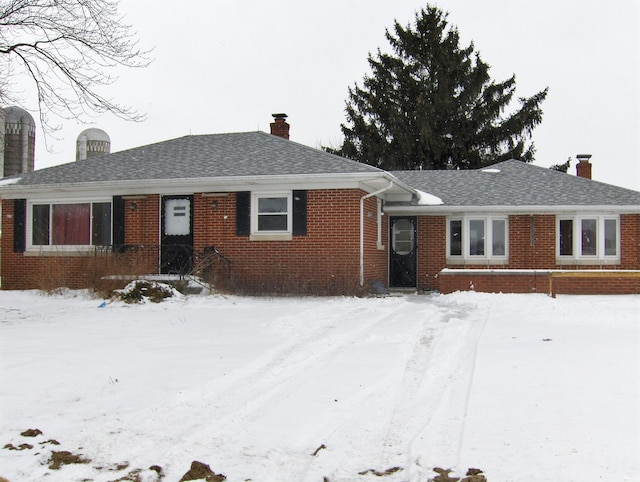 ranch-style house with brick siding, a chimney, and a shingled roof