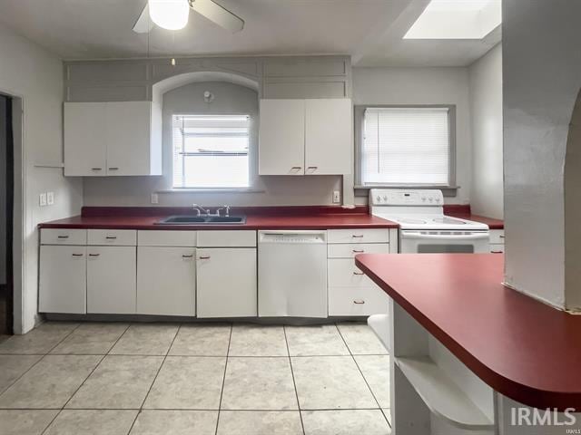 kitchen featuring white appliances, dark countertops, white cabinetry, a sink, and light tile patterned flooring