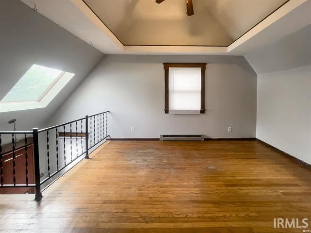 bonus room featuring lofted ceiling with skylight, ceiling fan, a baseboard heating unit, and light wood-style floors