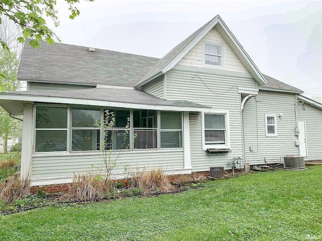 rear view of house with a sunroom, roof with shingles, cooling unit, and a yard