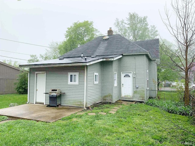 back of property featuring a chimney, fence, a lawn, and a patio