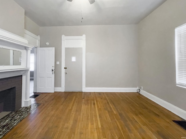 unfurnished living room with a brick fireplace, visible vents, baseboards, and wood finished floors