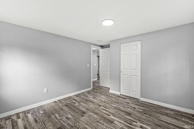 unfurnished bedroom featuring dark wood-type flooring, a closet, and baseboards