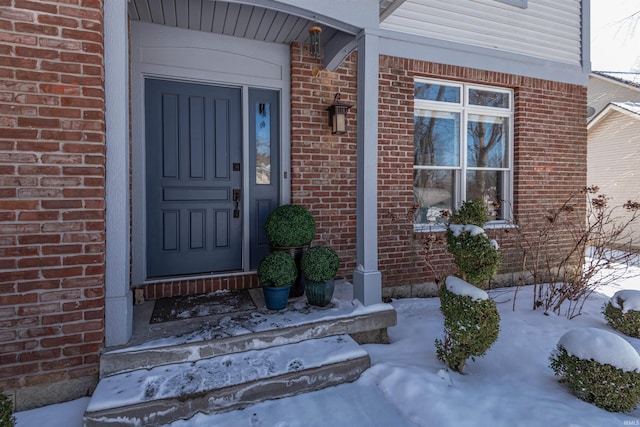 snow covered property entrance featuring brick siding