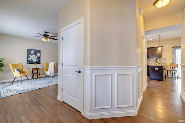 corridor with dark wood-style floors, a wainscoted wall, and baseboards